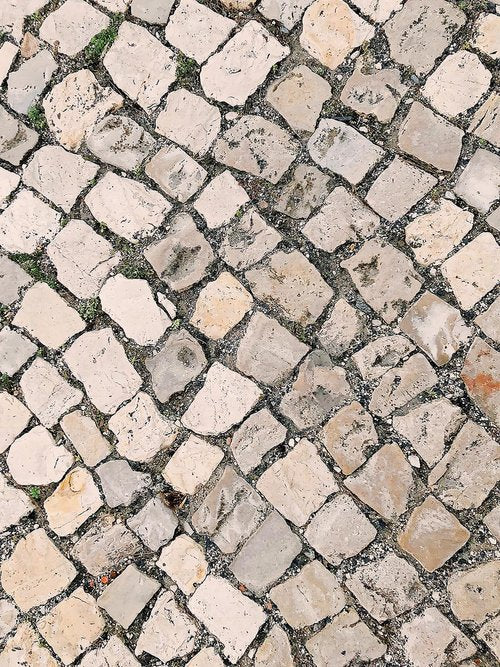 Diagonal pattern of uneven, light-colored cobblestones with patches of moss and dirt in between.