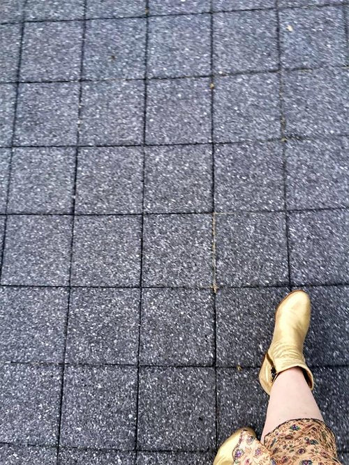 Person wearing golden boots and patterned pants walking on a gray tiled pavement with square grid pattern.