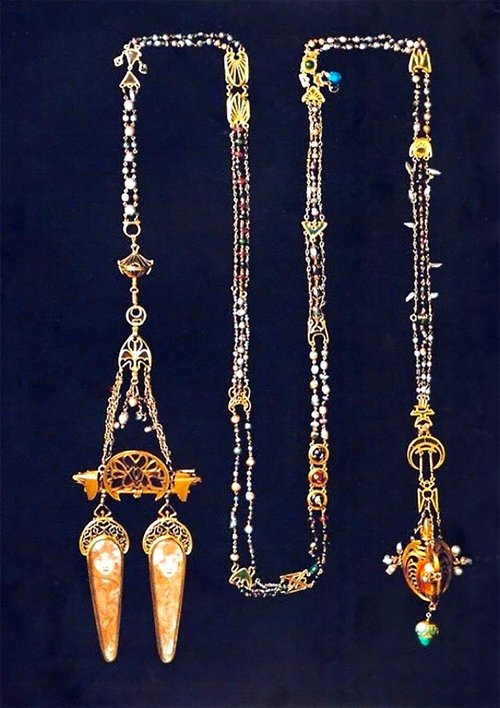Two ornate, antique-style necklaces with intricate gold elements, colorful beads, and elaborate pendants displayed against a black background.