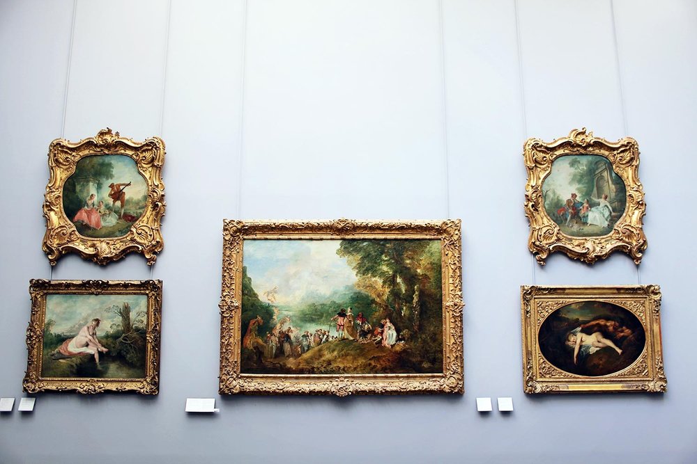 Wall display of five ornate-framed classical oil paintings in a museum or gallery, showcasing romantic and mythological scenes in a variety of shapes and sizes.